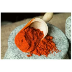 Wooden scoop of paprika being emptied on a stone