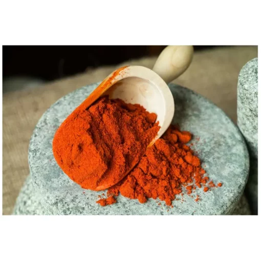Wooden scoop of paprika being emptied on a stone