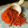 Wooden scoop of paprika being emptied on a stone