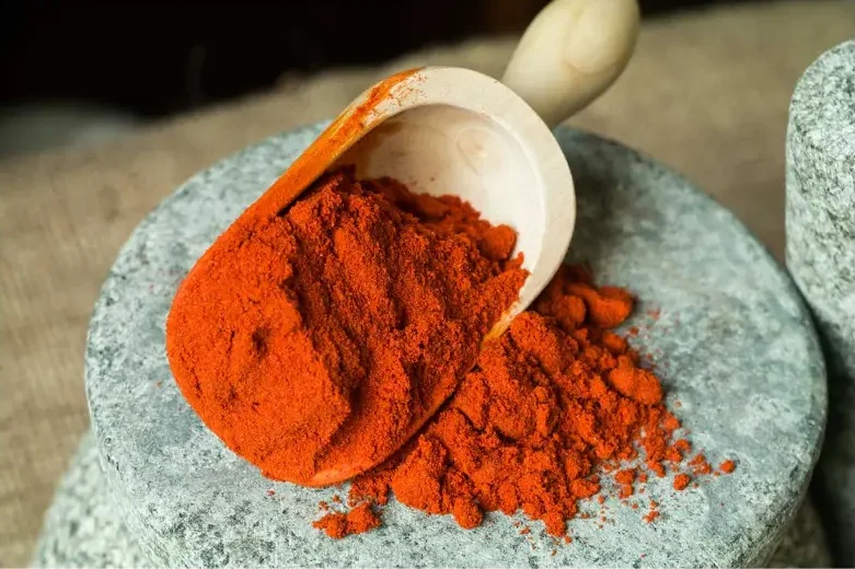 Wooden scoop of paprika being emptied on a stone