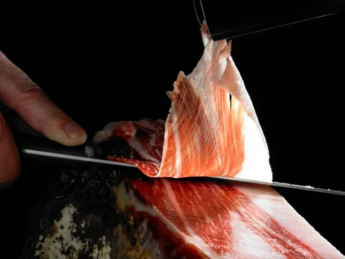 Closeup of knife cutting Iberian ham - Spanish gourmet